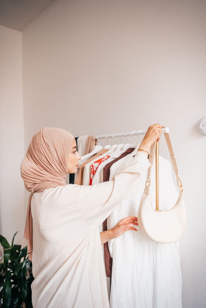 journey Stylish woman in hijab arranging clothes on a rack indoors.
